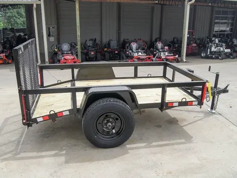 Short black utility trailer, open tube side rails, wood deck, mesh ramp gate lowered forward, single black steel wheel